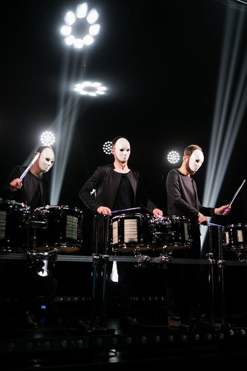 Three People with Masks Playing Drums