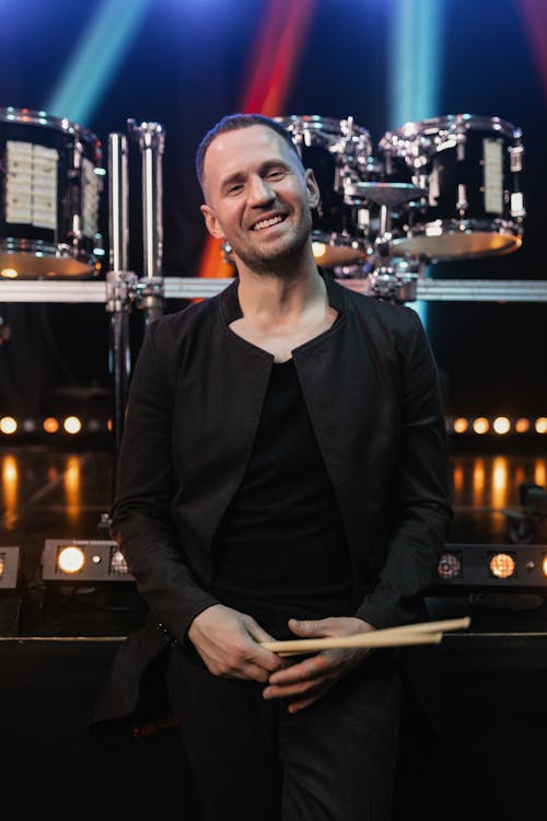 A Man in Black Long Sleeves Smiling while Holding a Drumsticks