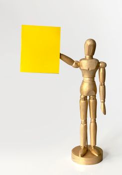 Wooden mannequin poses with a blank yellow paper for creative concept art.