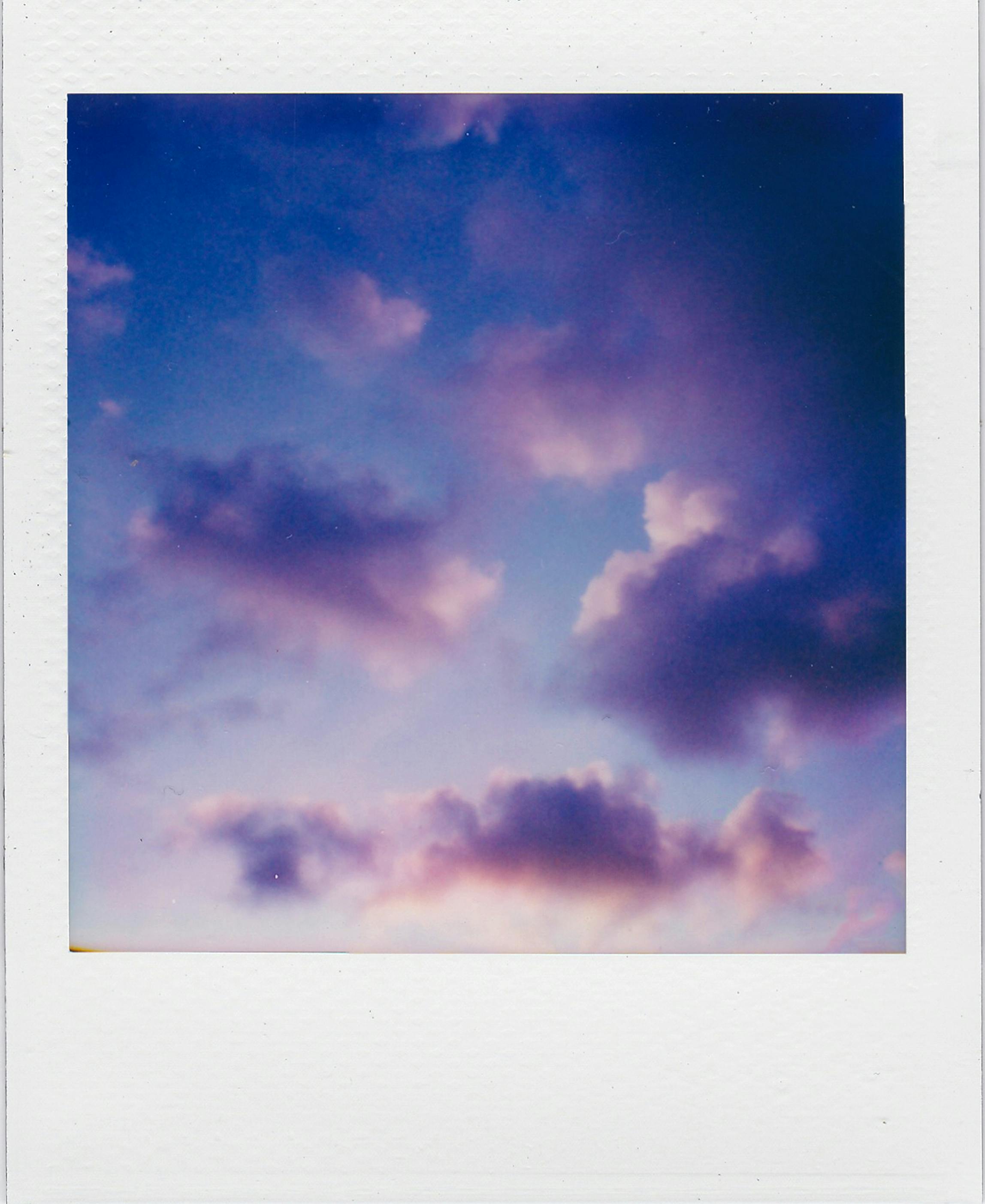 A dreamy sky with purple clouds at sunset captured in a classic polaroid frame, evoking nostalgic vibes.