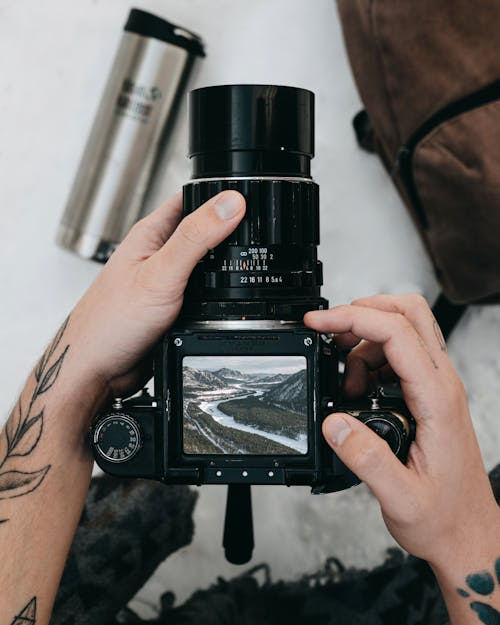 From above of crop anonymous tattooed photographer watching images of picturesque snowy mountains on screen of modern digital camera during trekking in nature