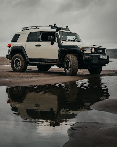Modern off road car parked on sandy shore of lake against overcast sky