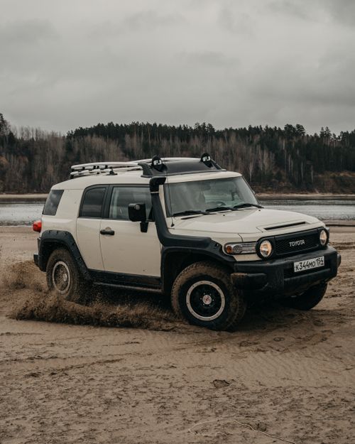 Free Modern SUV car driving on wild sandy beach near lake and lush green trees against gray cloudy sky Stock Photo