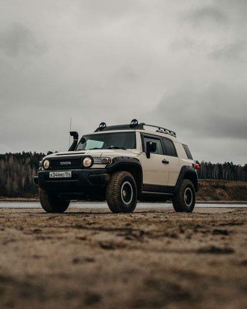 Free Ground level of contemporary offroader parked on sandy coast near sea and lush green forest under gray overcast sky Stock Photo