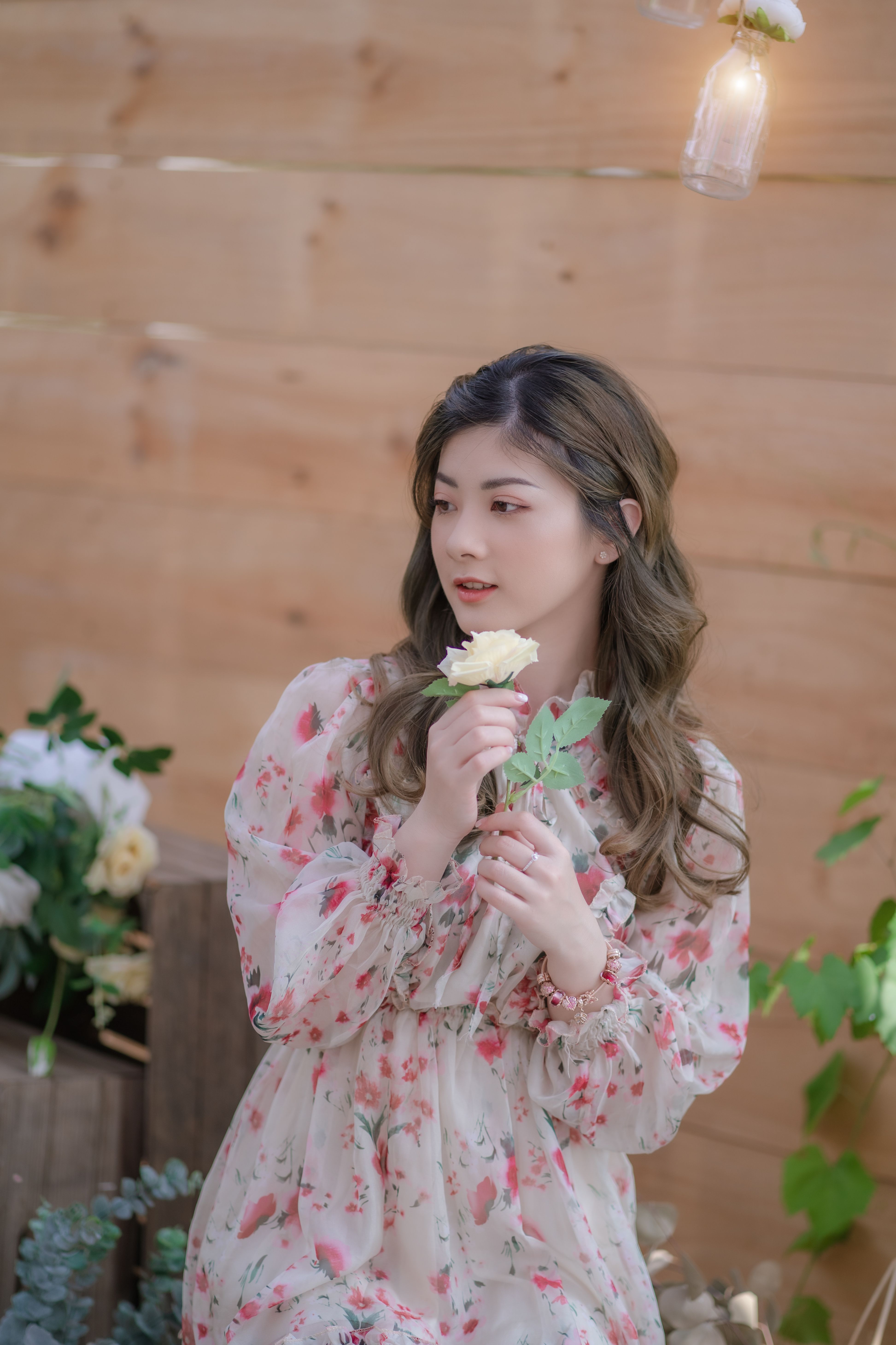 Asian girl in floral dress holding white rose in serene garden setting.