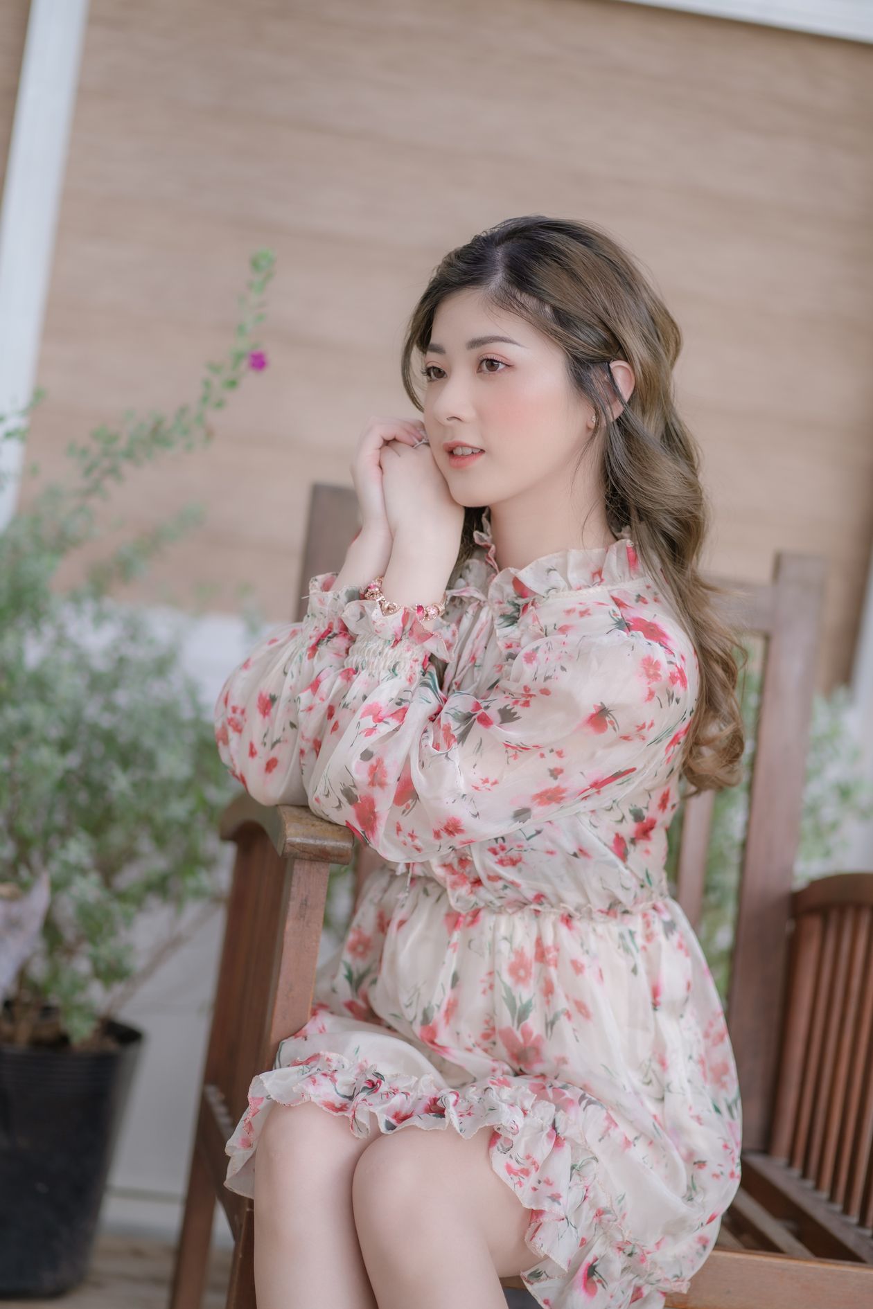 Woman in a white dress with red floral print sitting on a porch chair