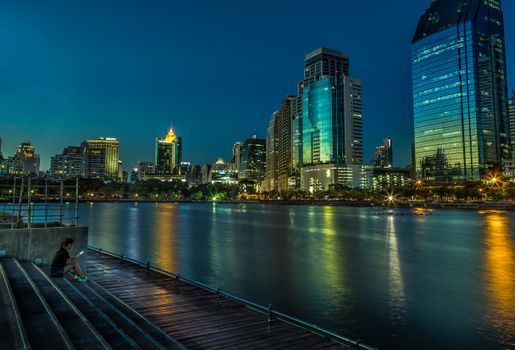 Stunning cityscape view of illuminated skyscrapers by water at Benjakitti Park.