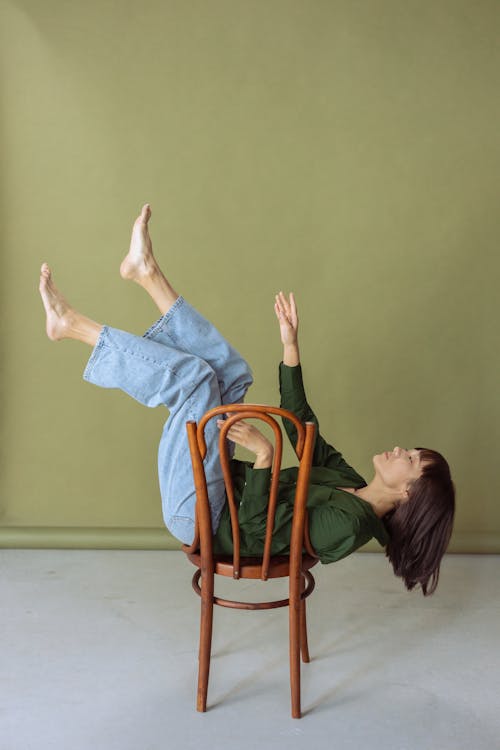 A Woman in Green Long Sleeves Lying on a Wooden Chair while Raising Her Feet