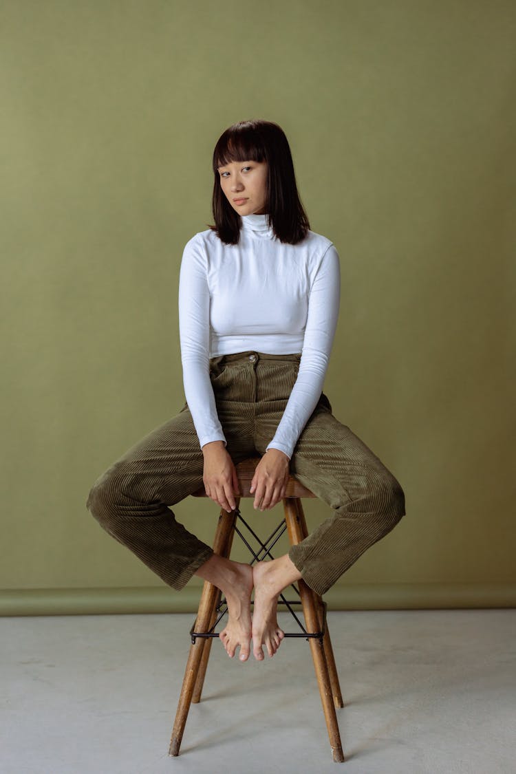 Woman In A White Long Sleeve Top Sitting On A Brown Wooden Stool