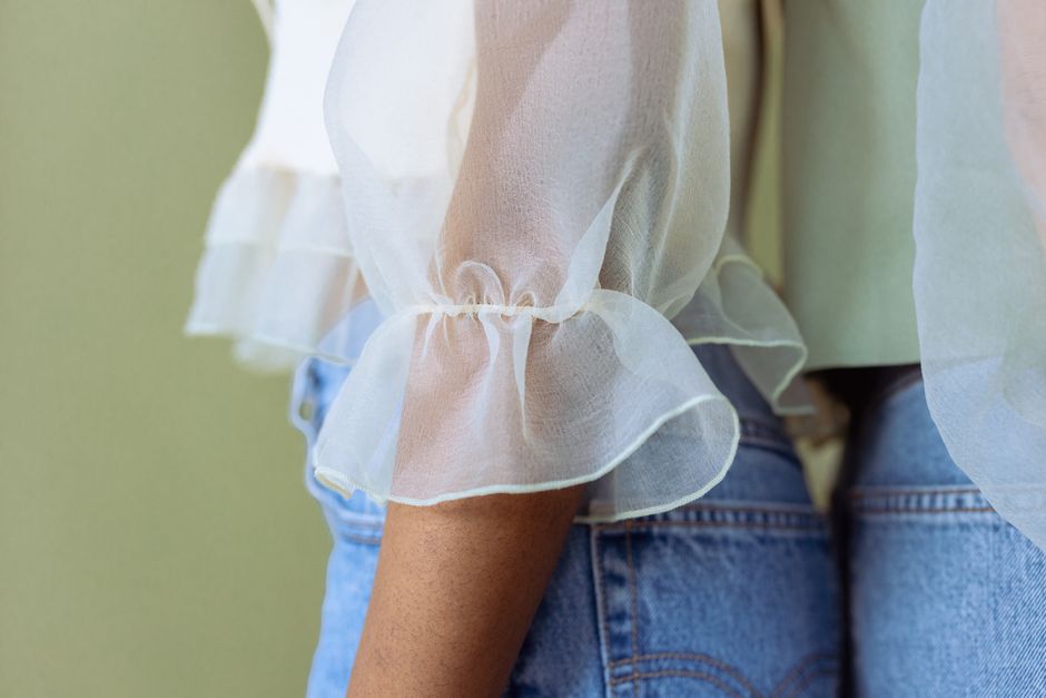 Close-up of a sheer white blouse with ruffles paired with denim jeans, showcasing modern fashion.
