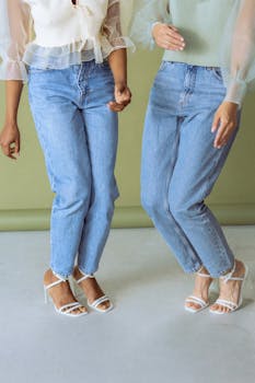 Two women in stylish blue jeans and white heels showcase modern fashion.