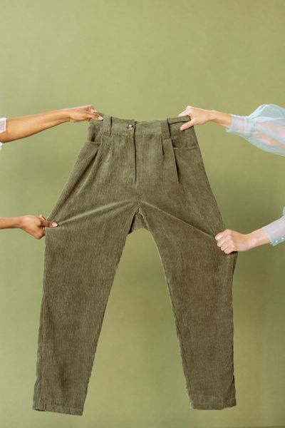 Olive corduroy wide-leg trousers held up against a green wall, photo by cottonbro studio on Pexels
