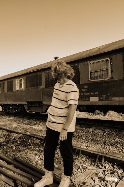 A Man in Striped Shirt and Black Pants Standing on the Railway