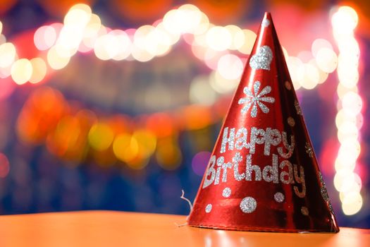 Bright red birthday party hat with glitter design, colorful bokeh lights.