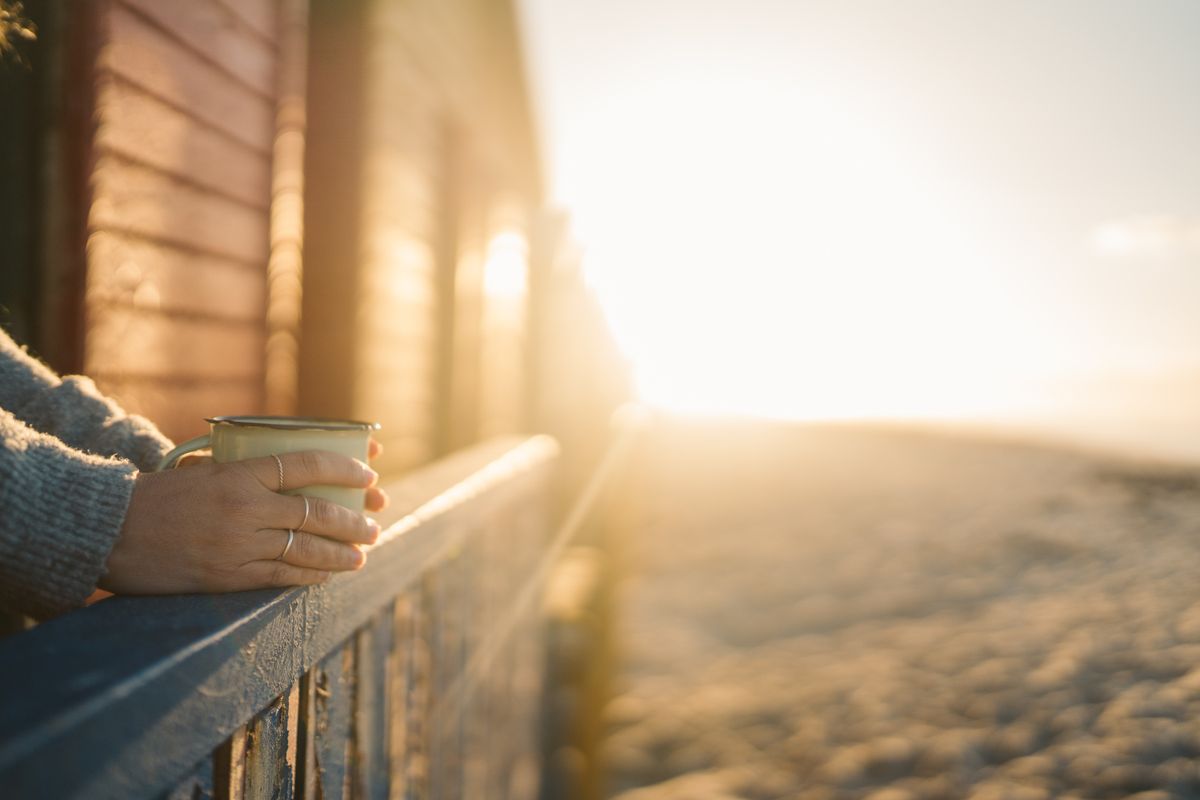 Eine Person hält eine Tasse Kaffee bei Sonnenaufgang