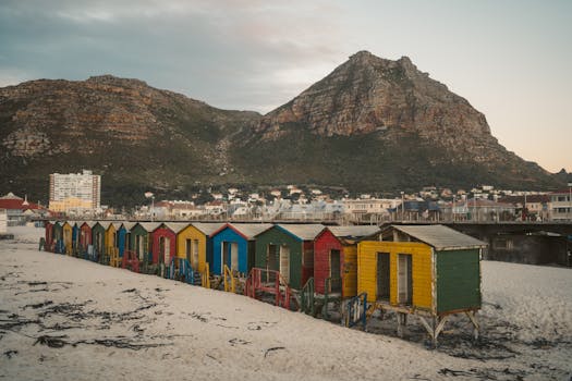 Vibrant beach huts line the shore against a rocky mountain backdrop, perfect for vacation memories.