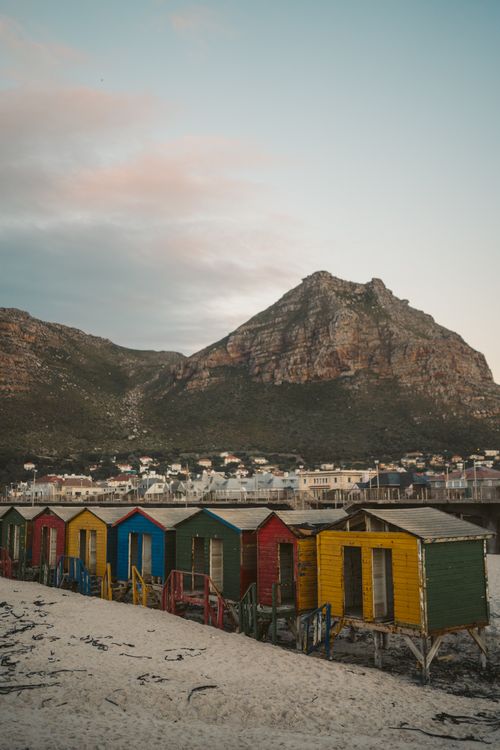 Free Vibrant wooden beach houses against a rocky mountain backdrop in Cape Town. Stock Photo