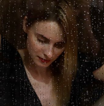 Portrait of a woman viewed through a rain-streaked window, capturing a moody and contemplative moment.