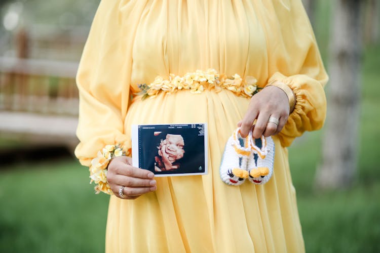 A Woman Holding Baby Shoes And A Sonogram