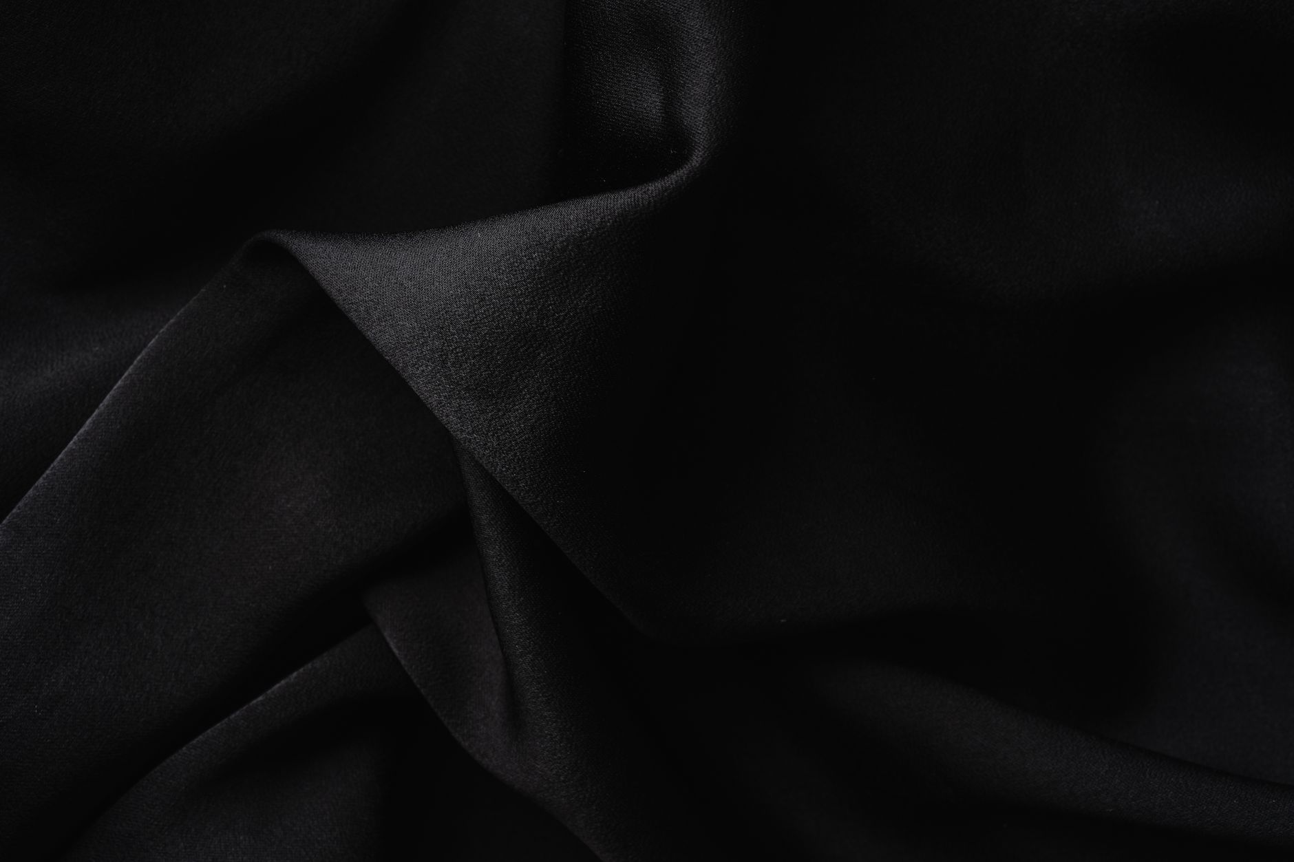 遮光窗簾價差從哪來?遮光等級、布料與做工全解說 Close-up of luxurious black fabric with soft, elegant folds creating a textured appearance.