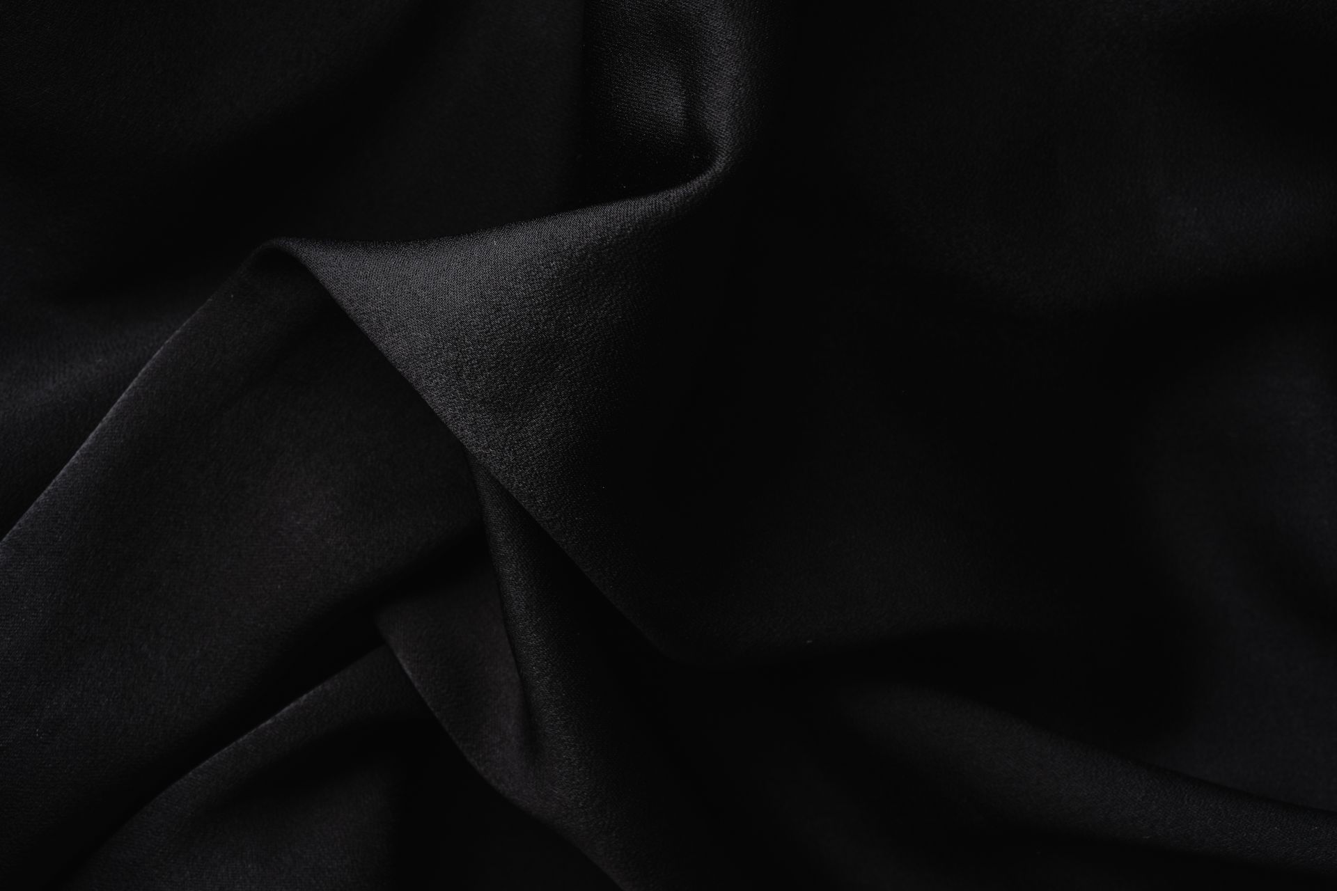 Close-up of luxurious black fabric with soft, elegant folds creating a textured appearance.