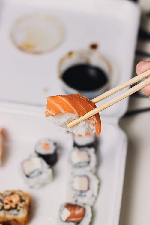 A Person Using Wooden Chopsticks on Salmon Sushi 