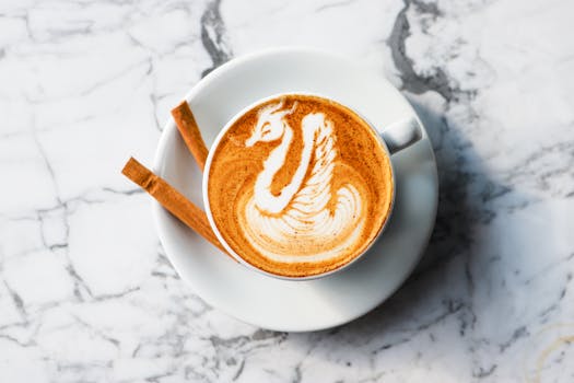 Artistic latte art in a cup of coffee with cinnamon sticks on a marble backdrop.