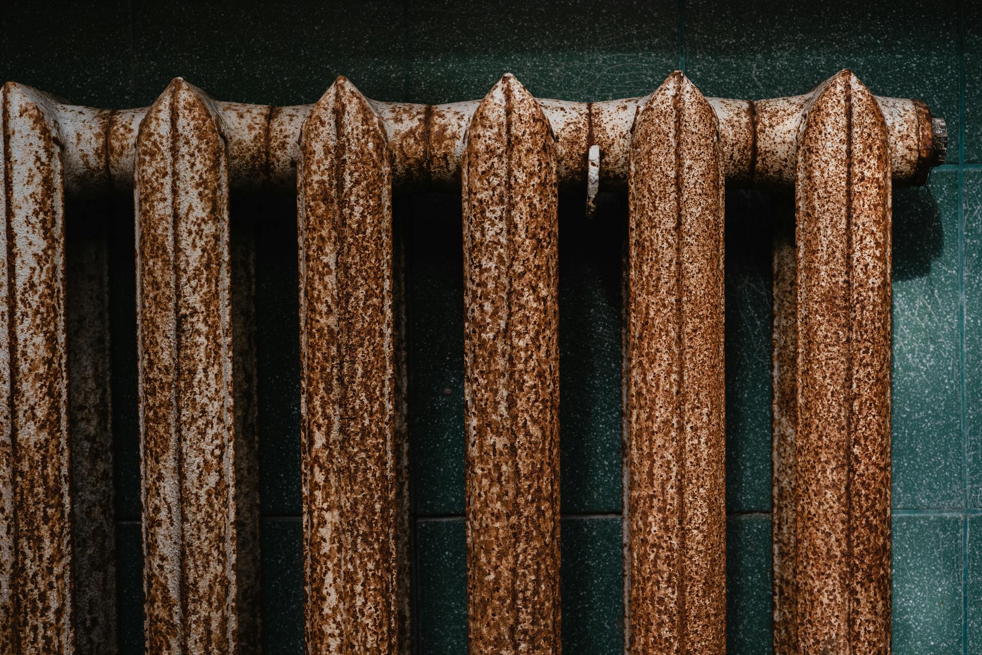 Close-up of a rusty old radiator with textured surface against green tiles, revealing industrial decay.