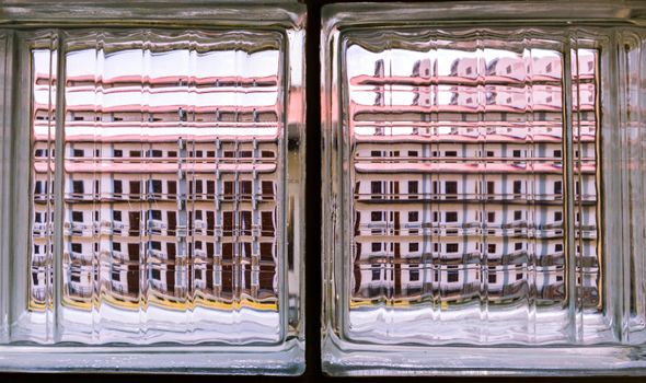 A building's reflection is distorted through clear glass brick blocks, creating an abstract urban view.