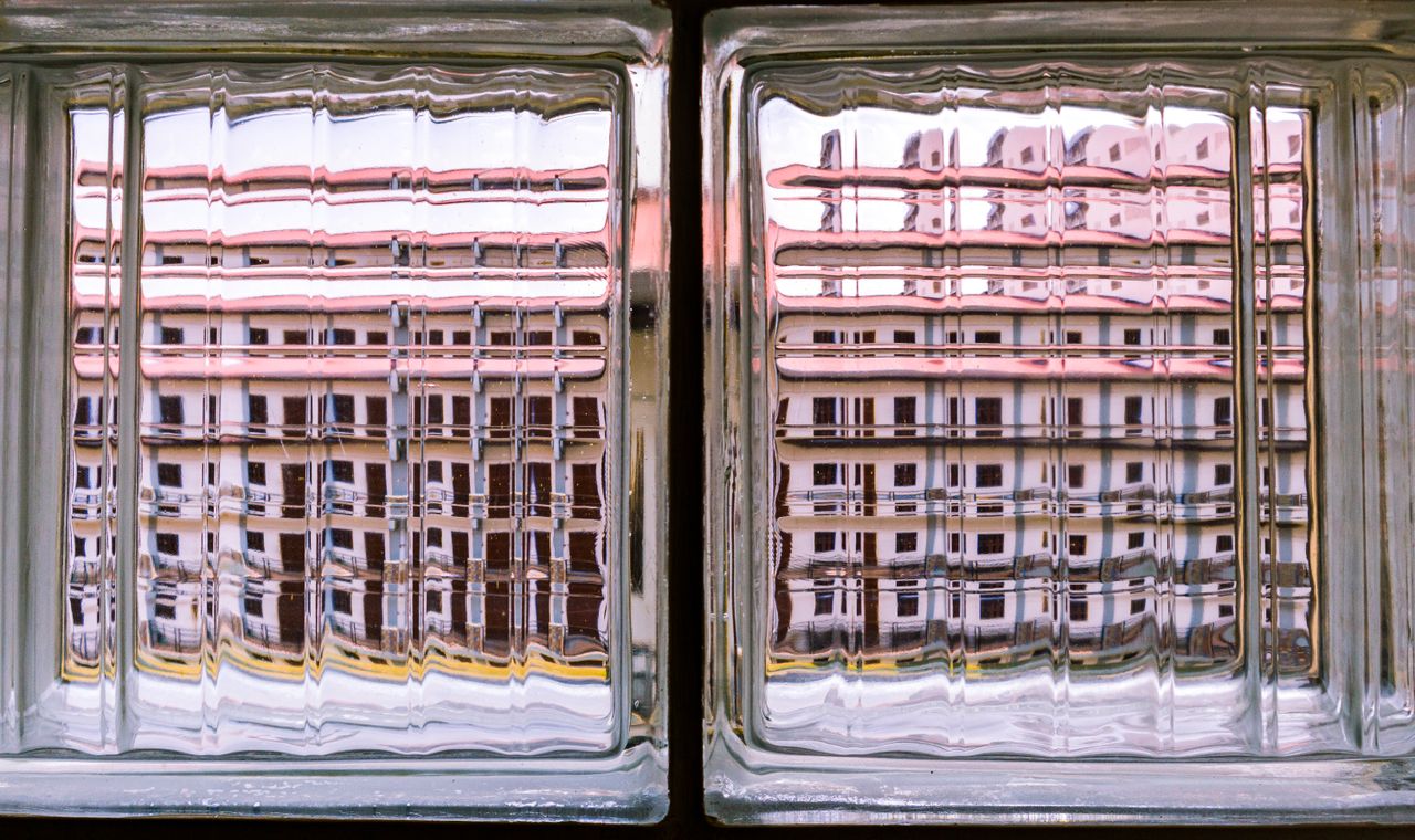 a building s reflection is distorted through clear glass brick blocks