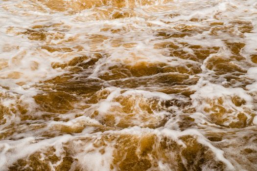 Close-up view of ocean waves crashing with brown seafoam and dynamic splashes.