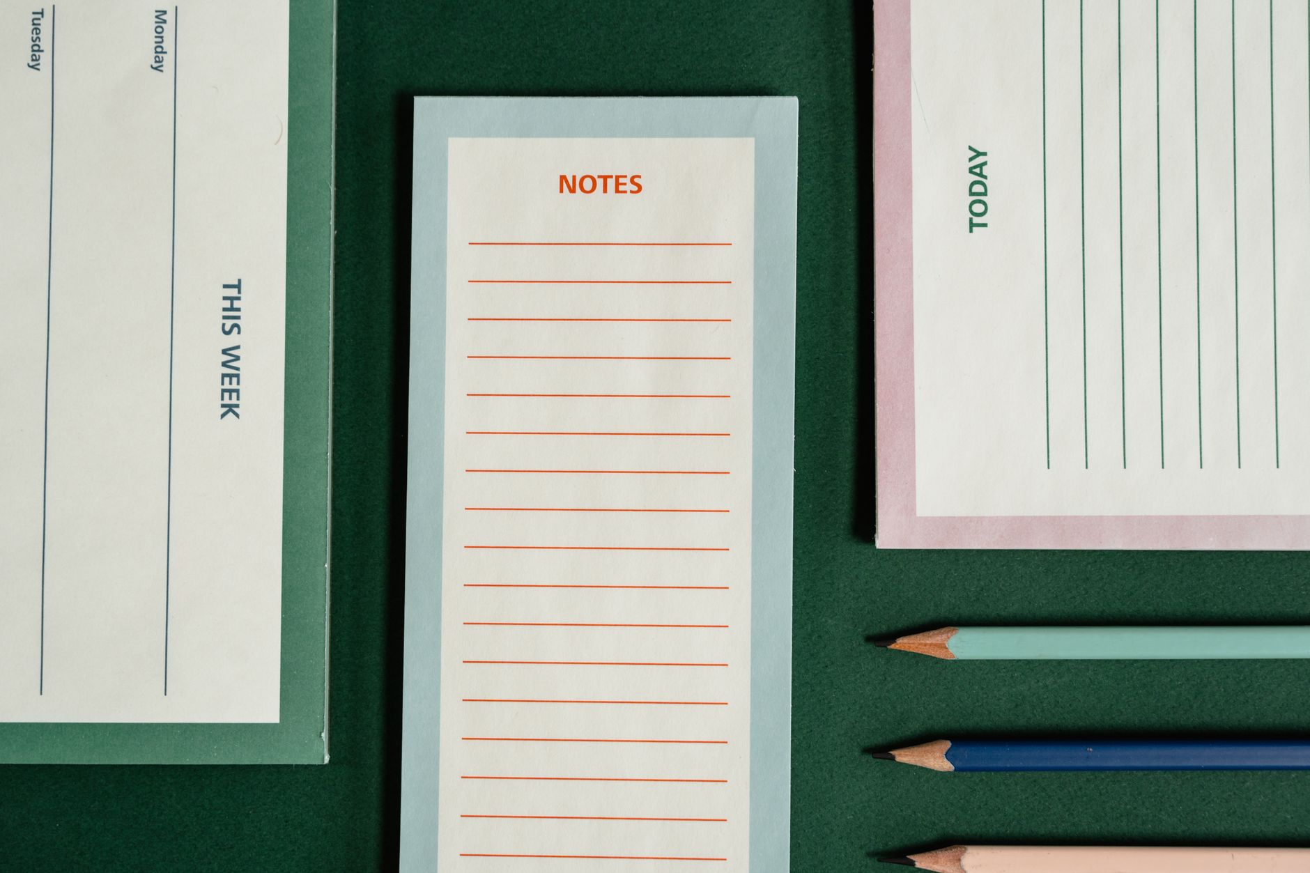 Organized flatlay featuring notepads and colored pencils on a green background.