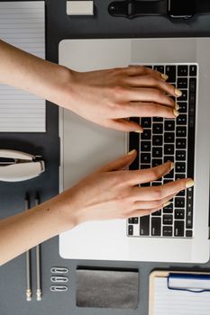 Overhead shot of manicured hands typing on a laptop, surrounded by office supplies.