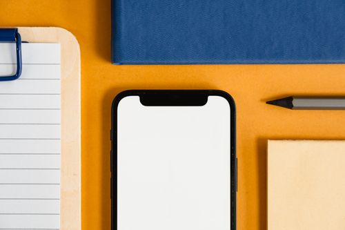 Free A flat lay of office supplies, including a smartphone, clipboard, pencil, on a vibrant orange desk. Stock Photo