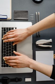 Hands with manicured nails typing on laptop keyboard in an organized workspace.