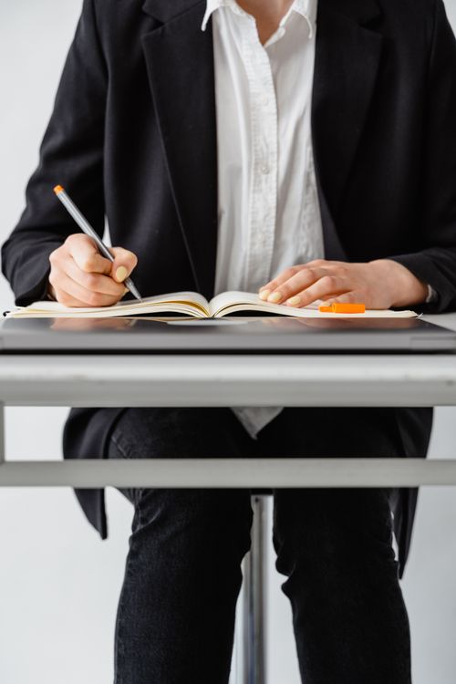 Free A woman in a suit writes notes in a notebook at a desk indoors. Stock Photo