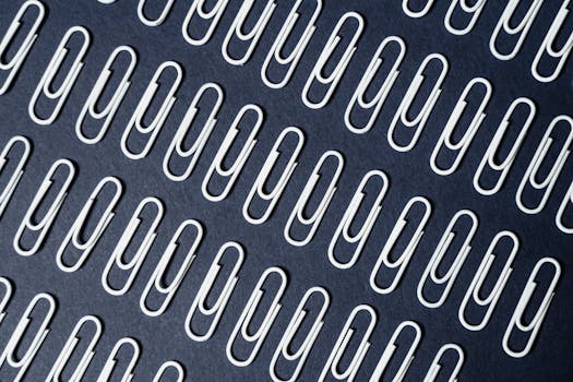 Close-up of neatly arranged paper clips on a dark surface creating a repeating pattern.