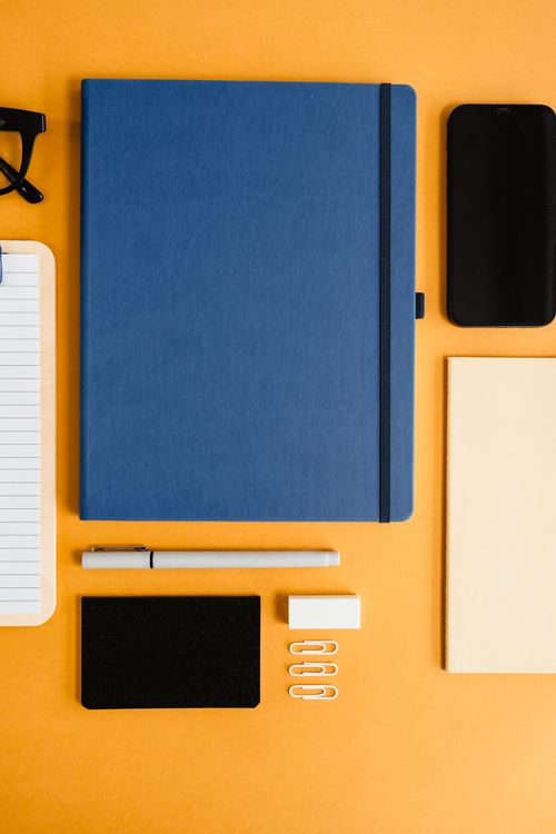 Free Stylish flat lay of office supplies including notebooks and stationery on a vibrant orange surface. Stock Photo
