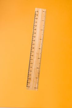 Close-up of a wooden ruler against a bright yellow surface. Ideal for school or office themes.
