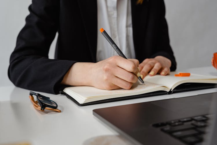 A Person Writing On A Planner