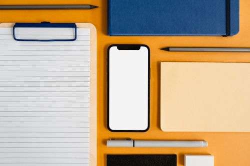Free A top view of office essentials including a smartphone, clipboard, and stationery on a yellow surface. Stock Photo