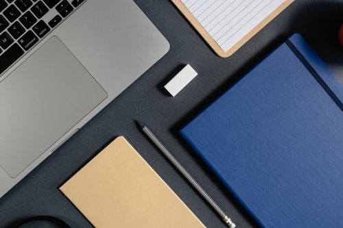 Free A minimalist top view of an office desk setup featuring a laptop, notebook, and stationery items. Stock Photo