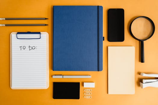 A top view of office stationery including a notebook, to-do list, and magnifying glass arranged on a yellow background.