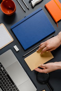 Flat lay of an organized workspace with office supplies and a laptop on a dark surface.