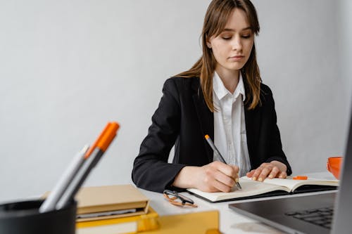 Woman Sitting by Desk Writing in Notebook