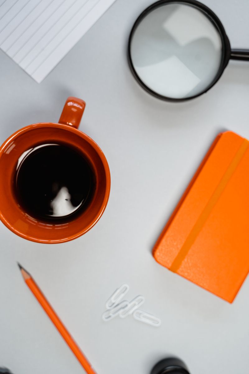 Overhead shot of orange coffee mug, notebook, and office supplies.