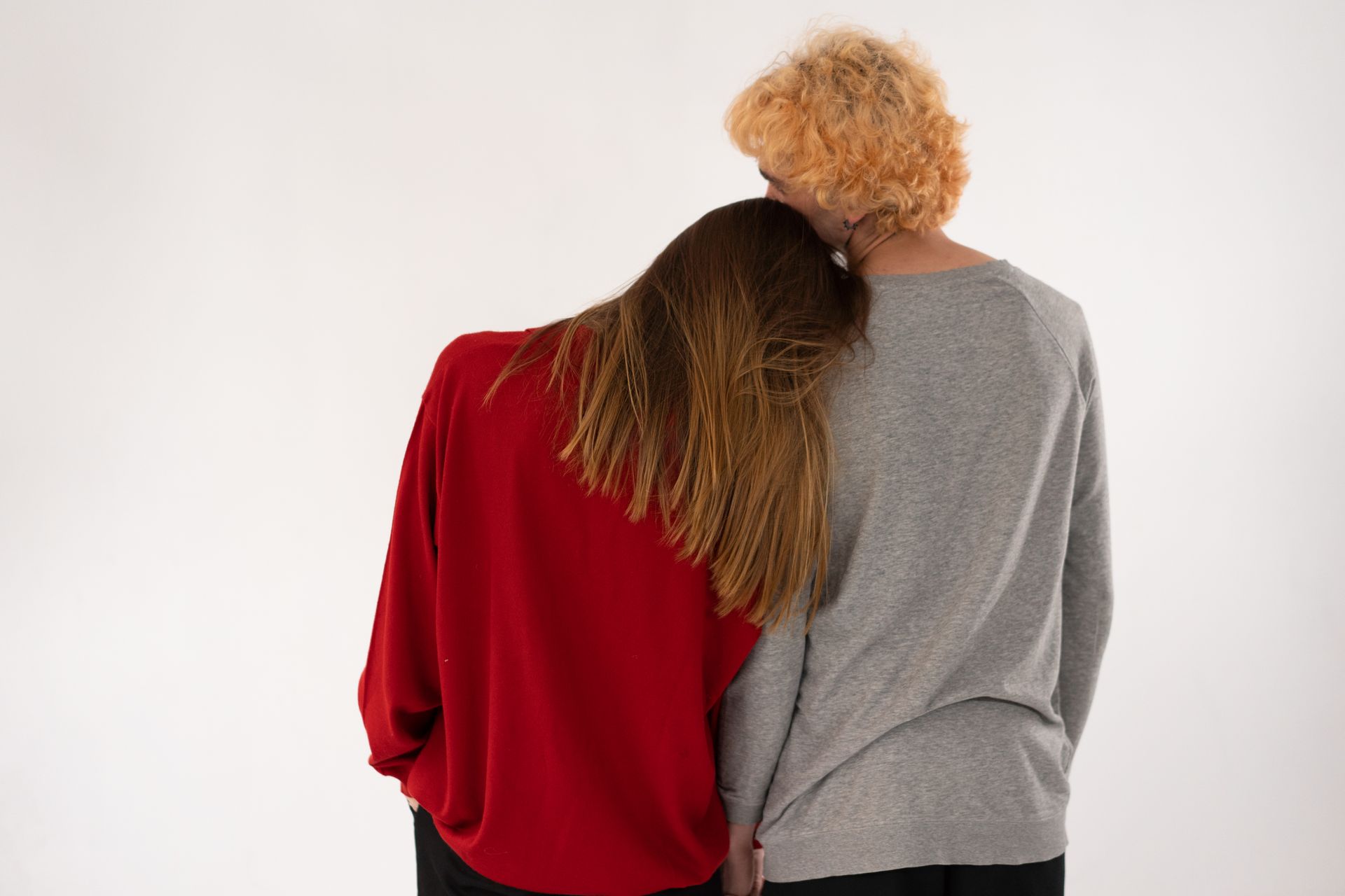 Two individuals express closeness, with one's head resting on the other's shoulder against a white background.