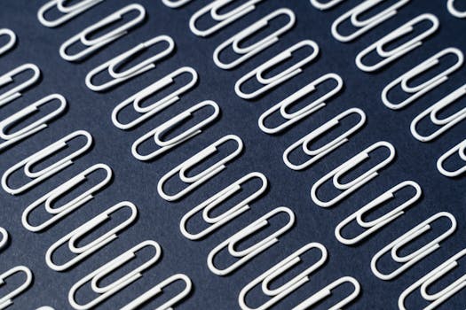 Perfectly arranged white paperclips on dark blue background showcasing minimalism.