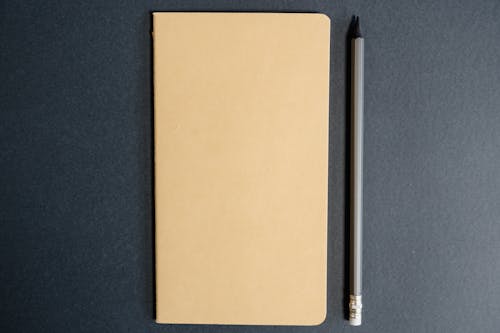 Notebook and Pencil Lying on Black Table
