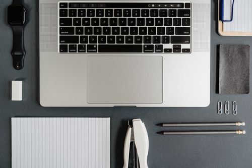 Free Top view of a sleek office desk with a laptop, notepad, smartwatch, and stationery essentials. Stock Photo